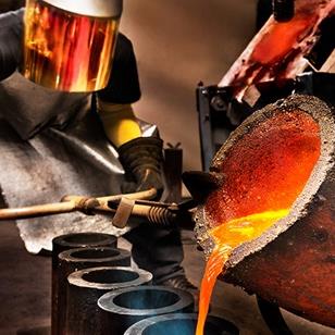 worker pouring molten steel into crucibles in a foundry