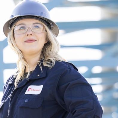 Woman wearing hard hat and glasses standing under a metal structure