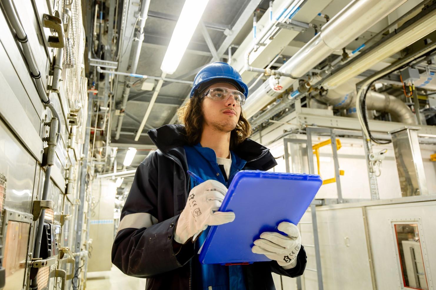 Employee in hardhat and safety glasses holding a clipboard
