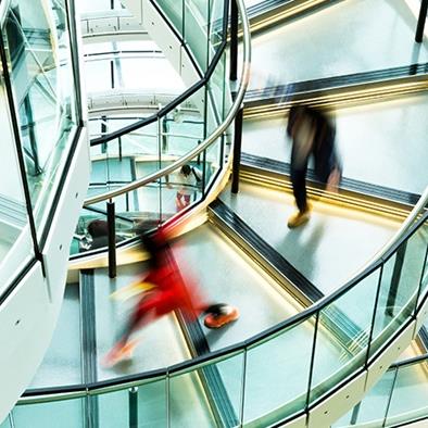 blurred figures walking down a modern steel and glass spiral staircase