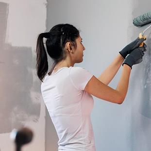 A woman wearing gloves painting wall, at home.