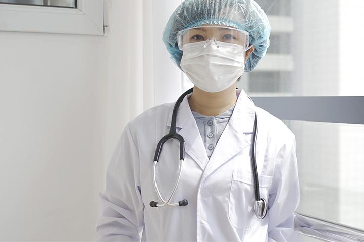 A woman in scrubs and PPE, standing in a hospital. 