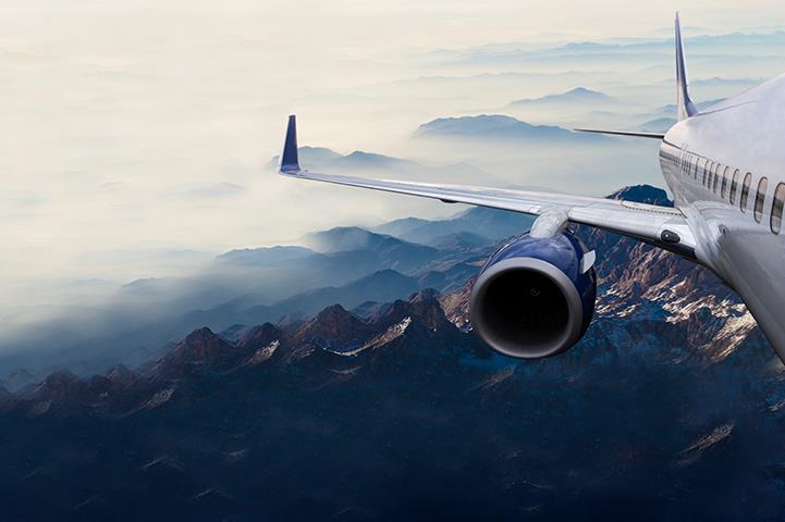 exterior shot of commercial airplane wing and engine flying over mountains