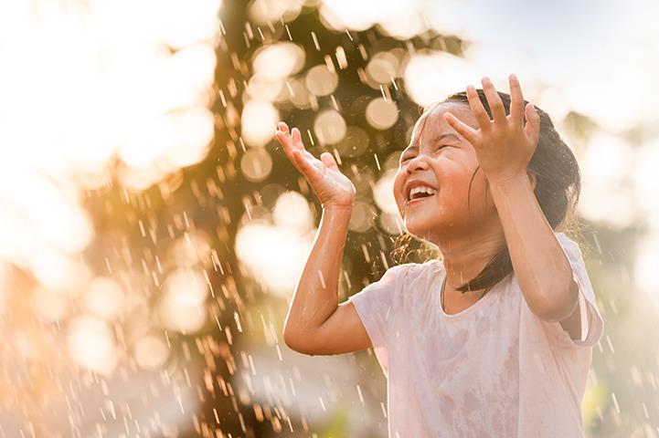 little girl holding hands up and laughing in a sun shower 