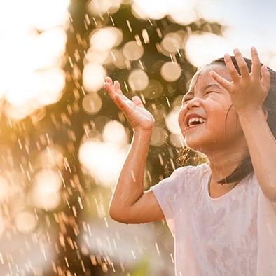 little girl holding hands up and laughing in a sun shower 