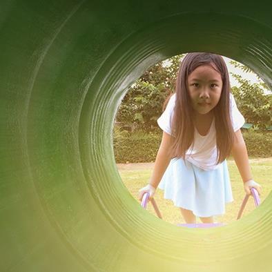 little girl standing in front of and looking into large green play equipment tube