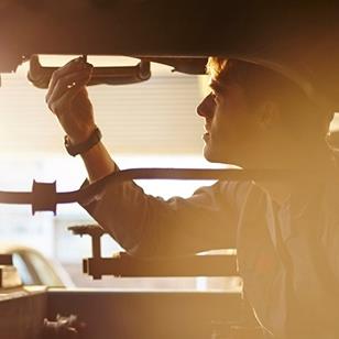 silhouette of mechanic working on underside of car