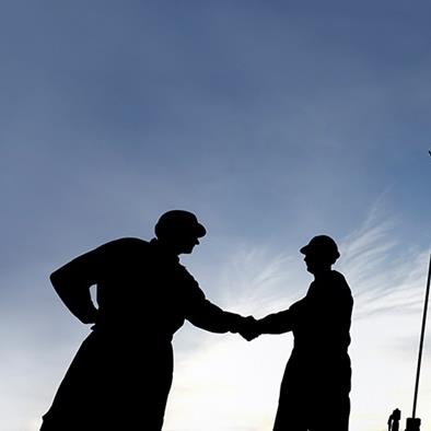 silhouette of two men shaking hands in front of oil machinery