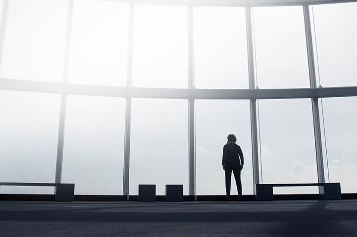 silhouetted person standing against a floor to ceiling bank of windows watching an airplane
