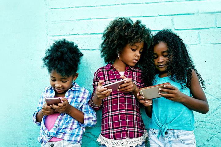 three girls standing against a blue wall looking at smart devices