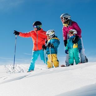 two adults and two children standing at the top of a ski slope
