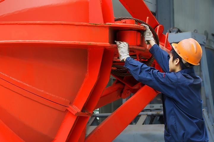 two workers in orange hardhats holding onto either side of large metal piece of equipment painted re