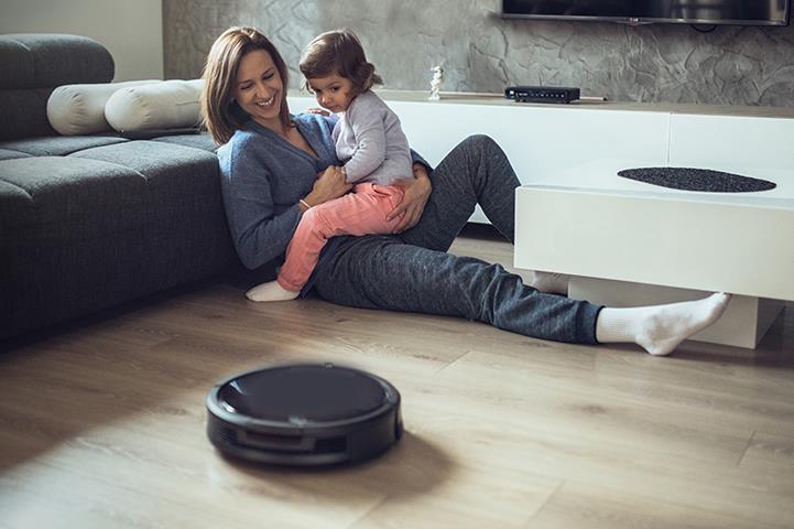 woman holding child on her lap both watching a robot vacuum