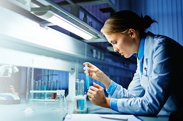woman in blue lab coat examining a test tube filled with blue liquid