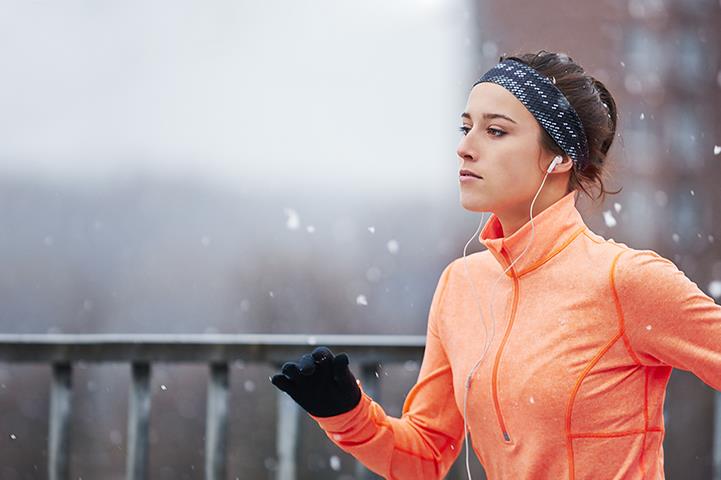 woman in orange jacket and black gloves running outside in snow