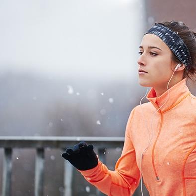 woman in orange jacket and black gloves running outside in snow