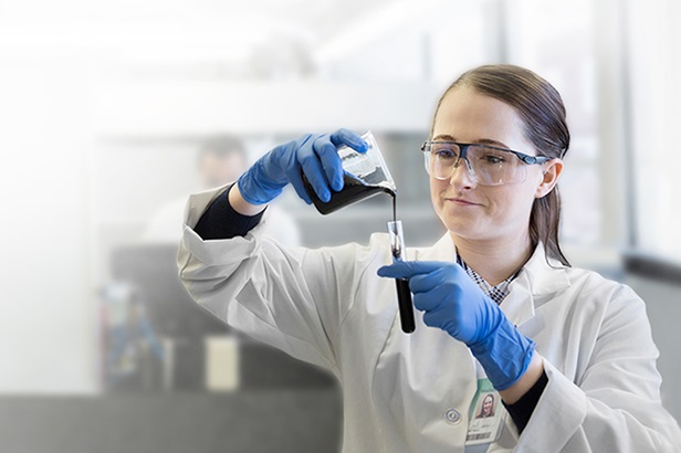 woman in white lab coat pouring liquid from beaker into test tube