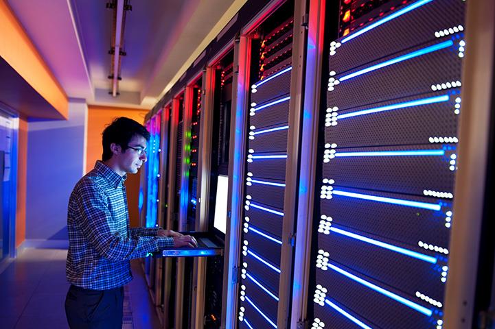 man typing on keyboard in datacenter room with wall of servers 