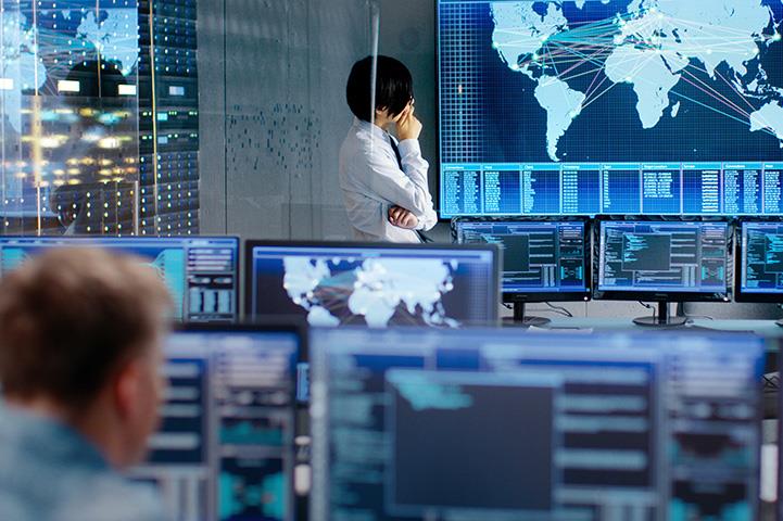 person in control room standing in front of large screen that is projecting a world map