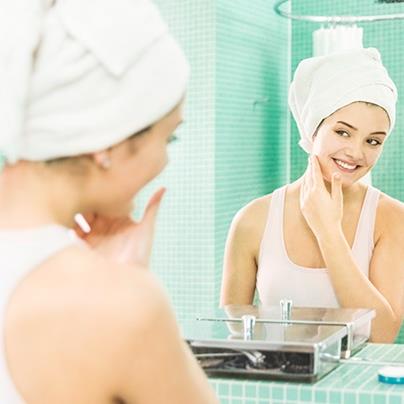 woman looking at self in mirror while applying lotion