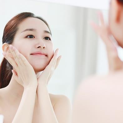 woman looking in mirror holding her face in her hands