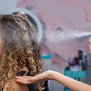 stylist spraying product on womans long hair at a salon 