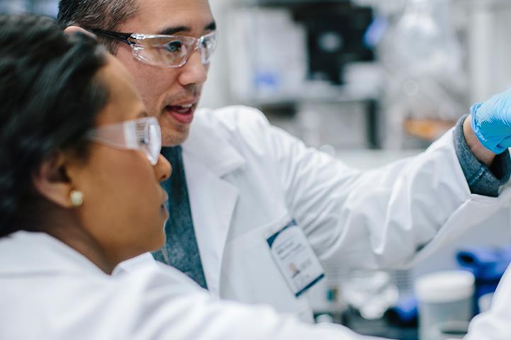 man and woman in white lab coats looking at test tubes in a laboratory