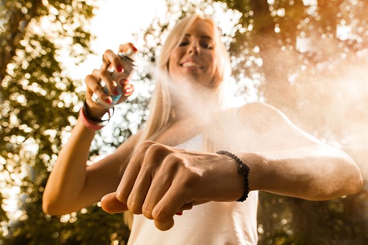 outside shot of woman in white tank top spraying repellent on her bare arm