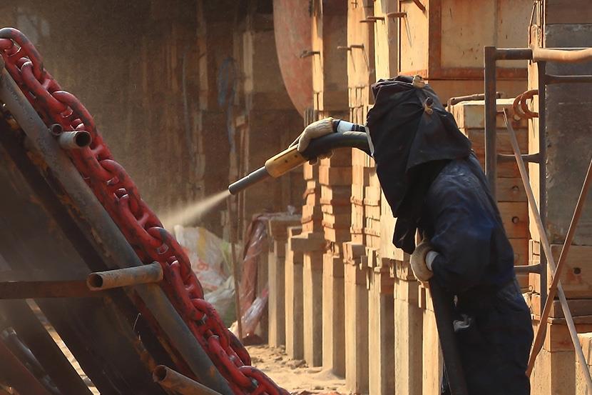 worker using abrasive blasting to clean large chains