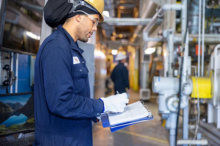 employee in hardhat writing on a clipboard