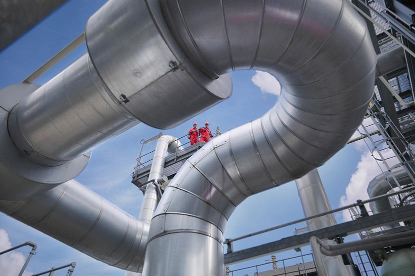 two people in red standing high and looking down on pipes at a gas storage plant