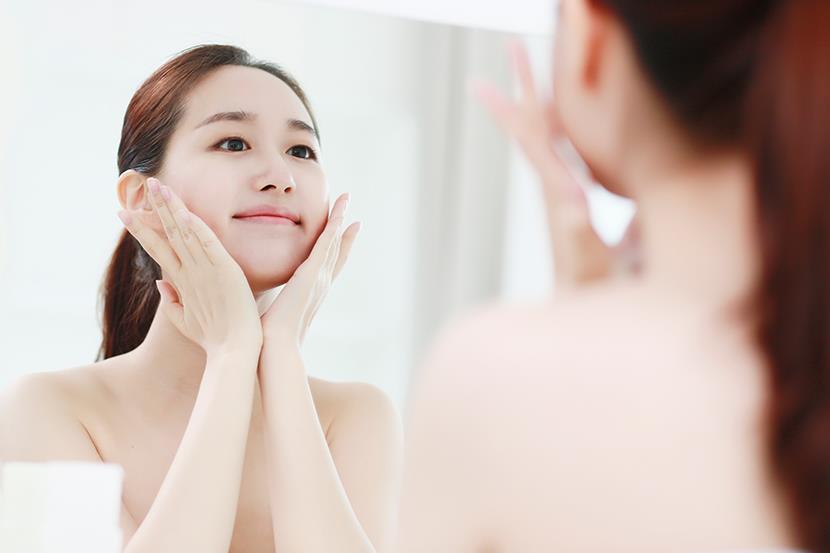 woman looking in mirror holding her face in her hands
