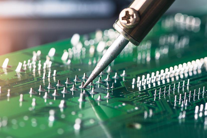 person soldering a green computer circuit board