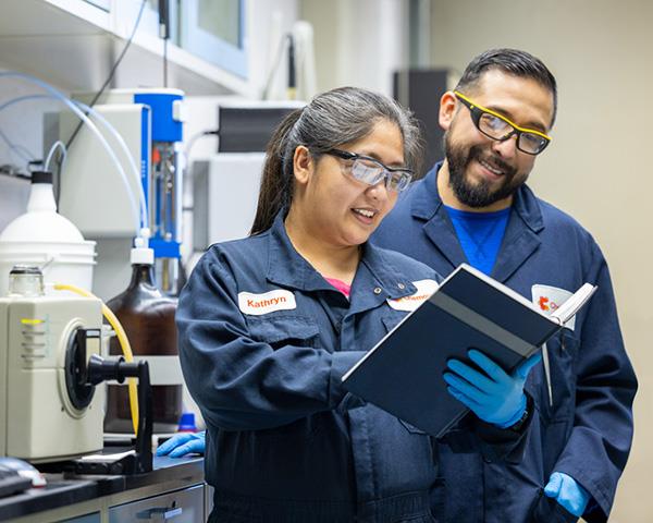 Two employees in safety glasses smiling at the camera