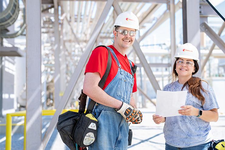 two employees earing hardhats and safety glasses smiling at the camera