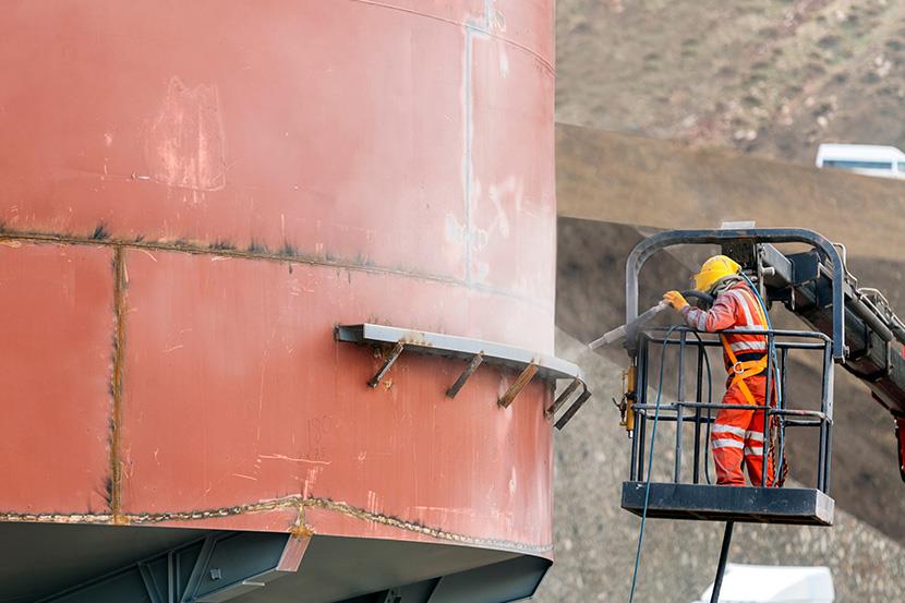 worker sandblasting the exterior of a steel tank