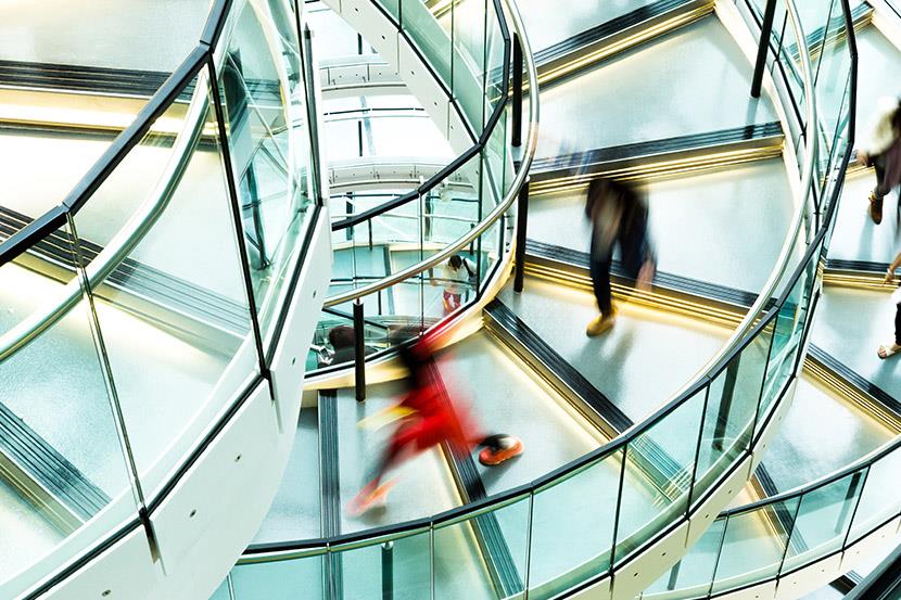 blurred figures walking down a modern steel and glass spiral staircase