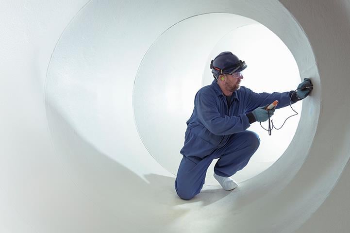 man in blue coveralls crouching inside large white turbine hall